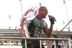 Foto do cantor Léo Santana em cima do trio elétrico do seu bloco no carnaval de Salvador, fantasiado de homem do futuro utilizando um braço mecânico